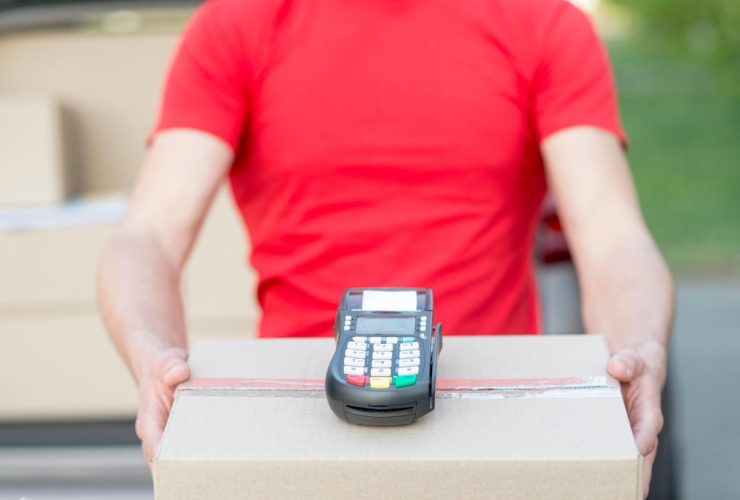 Pessoa segurando uma caixa de entrega e uma máquina de cartão nas mãos.